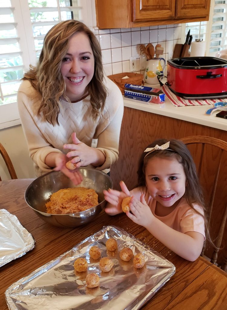 Young Woman rolling sausage dough with girl