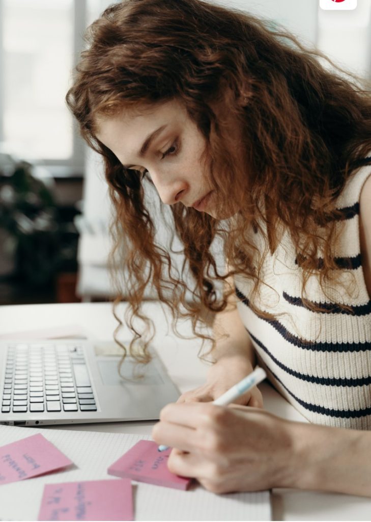 Woman writing notes near her laptop