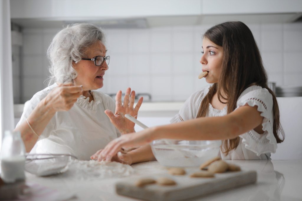 Older woman baking with teen girl eating cookie