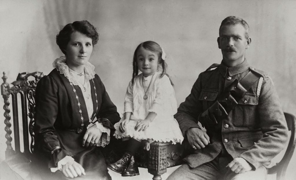 Black and white photo of women in early 20th century dress, small girl in white dress, husband in military uniform