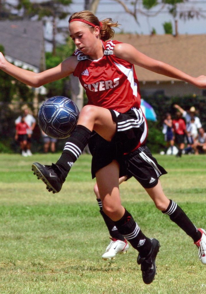 Photo of teen girl dribbling soccer ball during competition