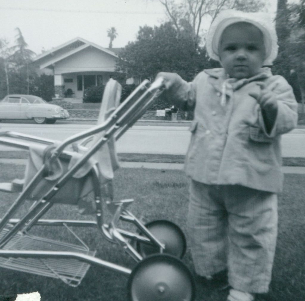 B&w photo of toddler with stroller in front of house